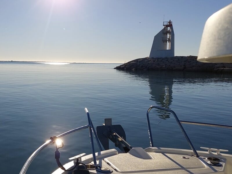Vue depuis un bateau approchant un phare moderne sur une digue par temps calme.