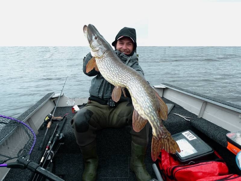 Pêcheur souriant tenant un grand brochet dans un bateau sur le lac de Naussac.