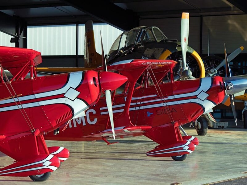 Deux avions de voltige rouge et blanc stationnés dans un hangar à l'aérodrome Jean-Baptiste Salis.