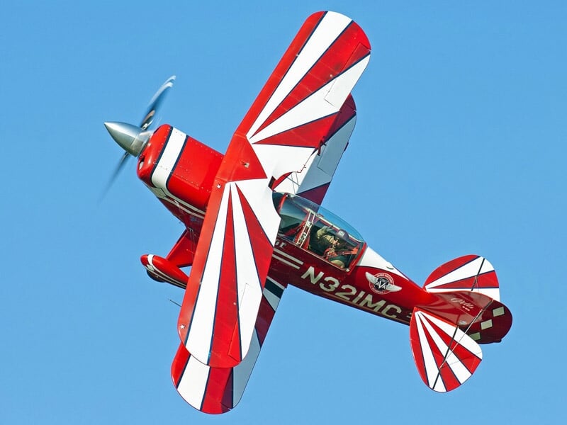 Avion de voltige rouge et blanc en plein vol avec un ciel bleu en arrière-plan.