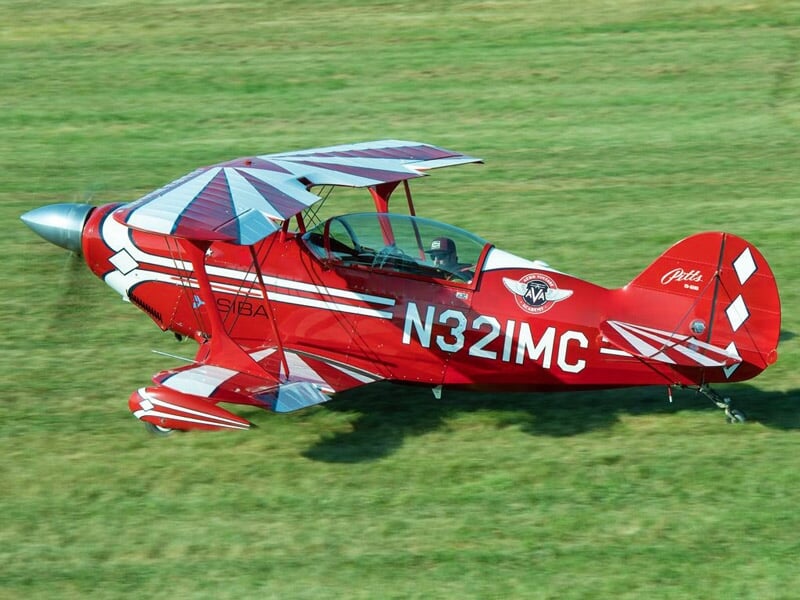 Avion de voltige rouge et blanc au sol sur une piste d'herbe, prêt au décollage.