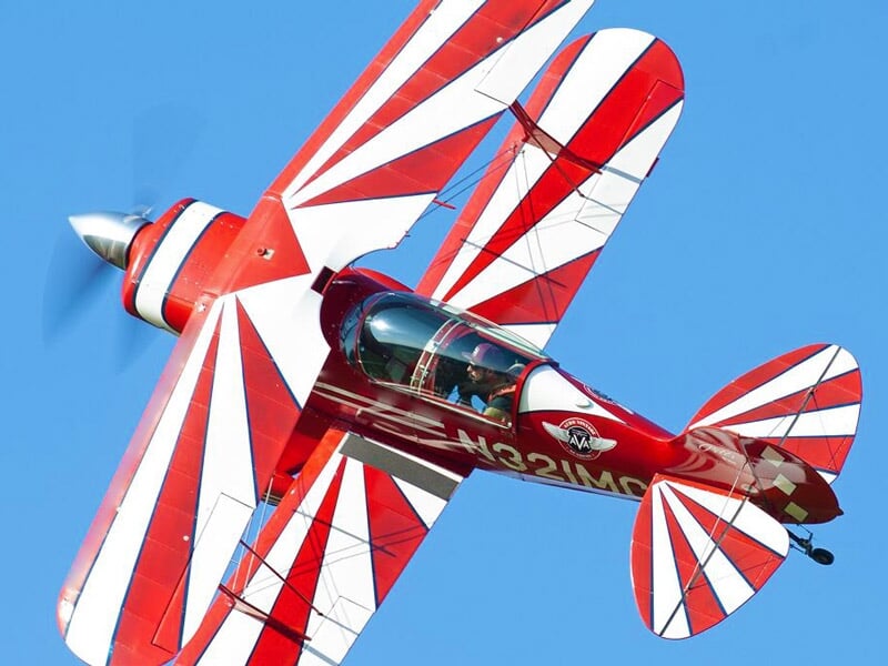 Avion de voltige rouge et blanc effectuant une figure acrobatique en vol au-dessus du ciel bleu.