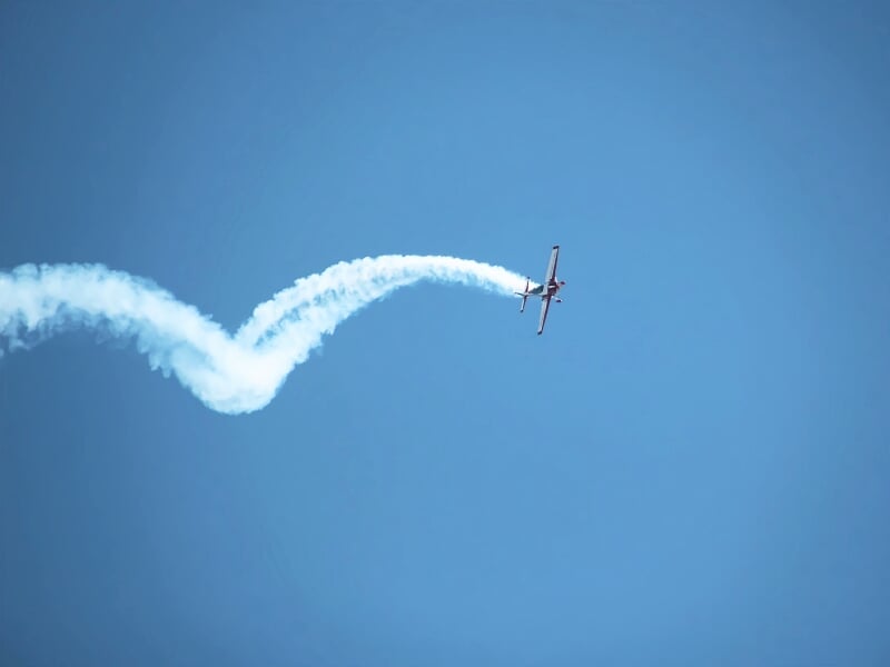 Avion de voltige effectuant une figure acrobatique dans un ciel bleu avec une traînée de fumée blanche.