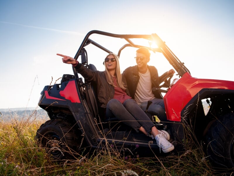 Un couple souriant dans un quad rouge, assis dans l'herbe avec le soleil couchant en arrière-plan.