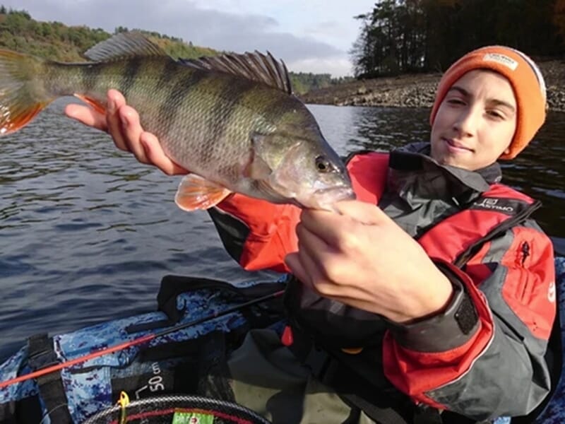 Jeune pêcheur en float-tube présentant une perche sur un lac avec une forêt en arrière-plan