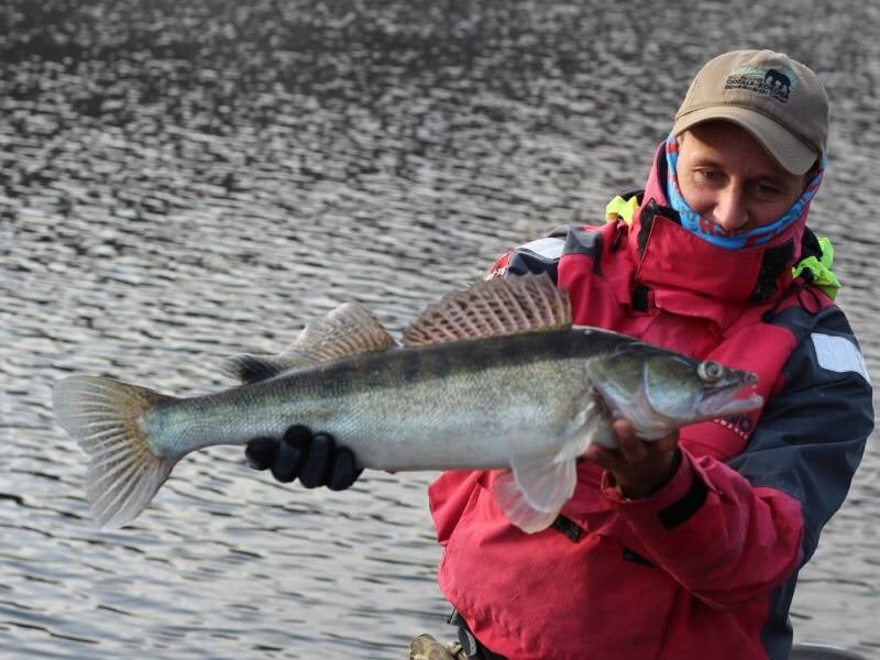 Personne en tenue de pêche rouge tenant un gros poisson au bord de l'eau lors d'un stage street-fishing près de Vannes.