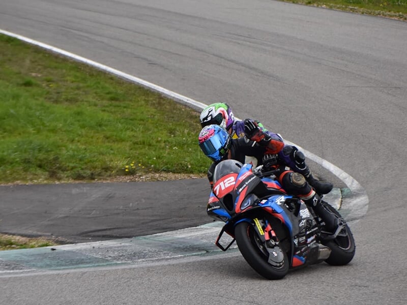 Moto numéro 712 en pleine courbe sur un circuit, avec deux pilotes inclinés et coordonnés, portant des combinaisons et casques de couleurs vives.