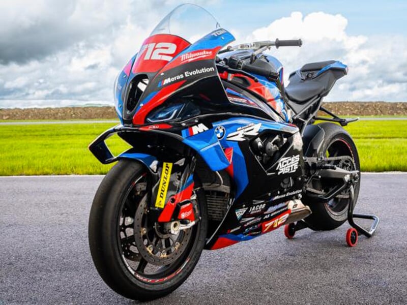 Moto numéro 712 en stationnement, mise en valeur sur une piste avec une vue dégagée sur l'herbe et le ciel, montrant les sponsors et détails de conception.