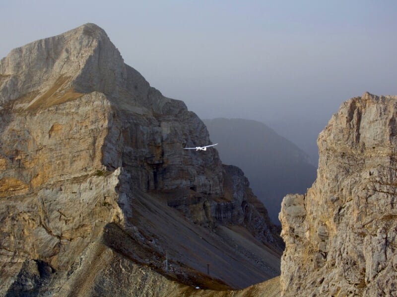 Planeur volant entre deux grandes falaises rocheuses dans un paysage montagneux sous un ciel clair.