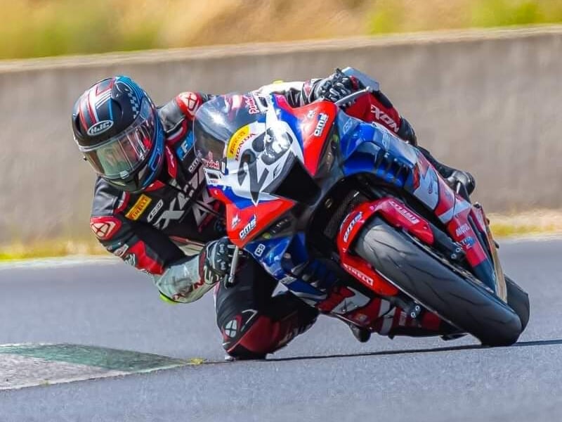 Motard en combinaison noire, rouge et bleue penché sur une moto de course assortie, négociant un virage avec précision sur piste sèche
