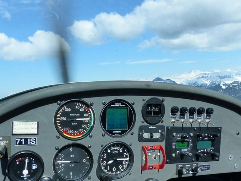 Tableau de bord d'un planeur en vol avec instruments visibles et ciel bleu avec montagnes enneigées au loin.