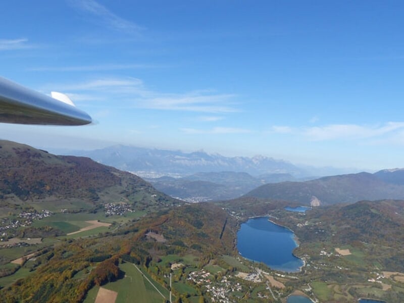 Vue aérienne depuis un planeur montrant un lac entouré de collines et montagnes sous un ciel clair.