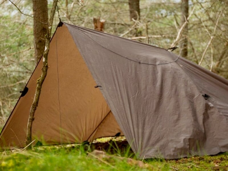 Tente de survie installée dans une forêt, abri simple en toile marron pour protection contre les éléments.