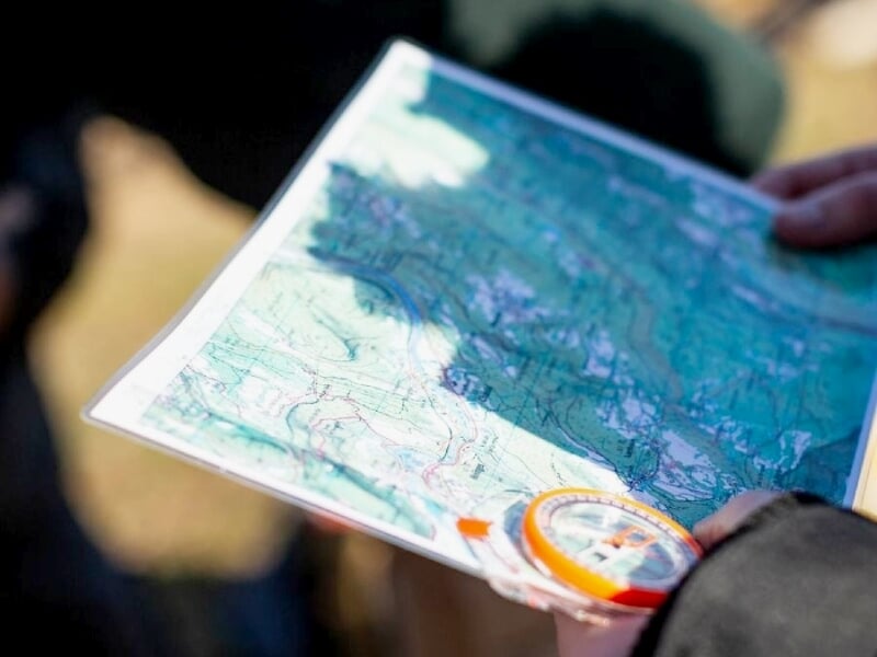 Carte topographique tenue à la main avec une boussole orange, utilisée pour s'orienter en pleine nature.