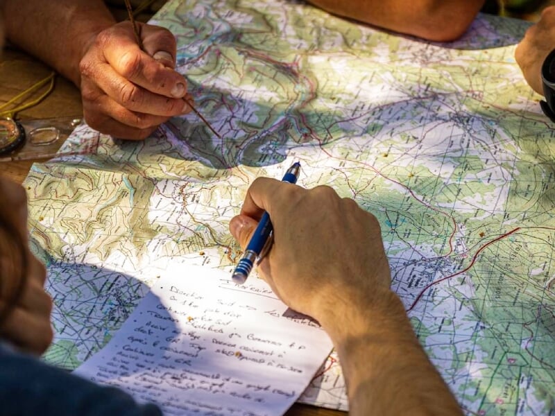 Gros plan sur des mains traçant un itinéraire sur une carte étalée, planification en plein air.