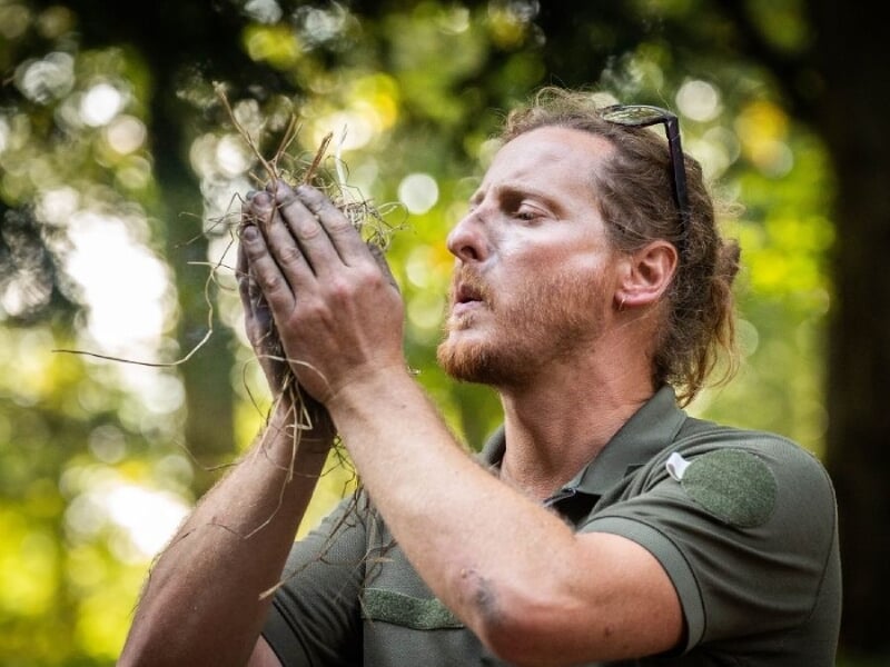 Homme soufflant sur un petit tas de brindilles pour allumer un feu, démonstration de technique de survie.