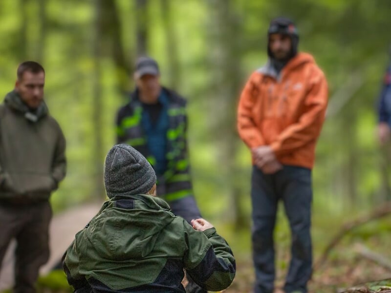 Personne assise au premier plan, entourée de plusieurs autres personnes en tenue de randonnée dans une forêt verdoyante.