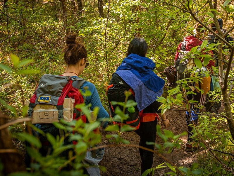 Groupe de randonneurs avec de grands sacs à dos traversant un lit de rivière rocheux en pleine nature.