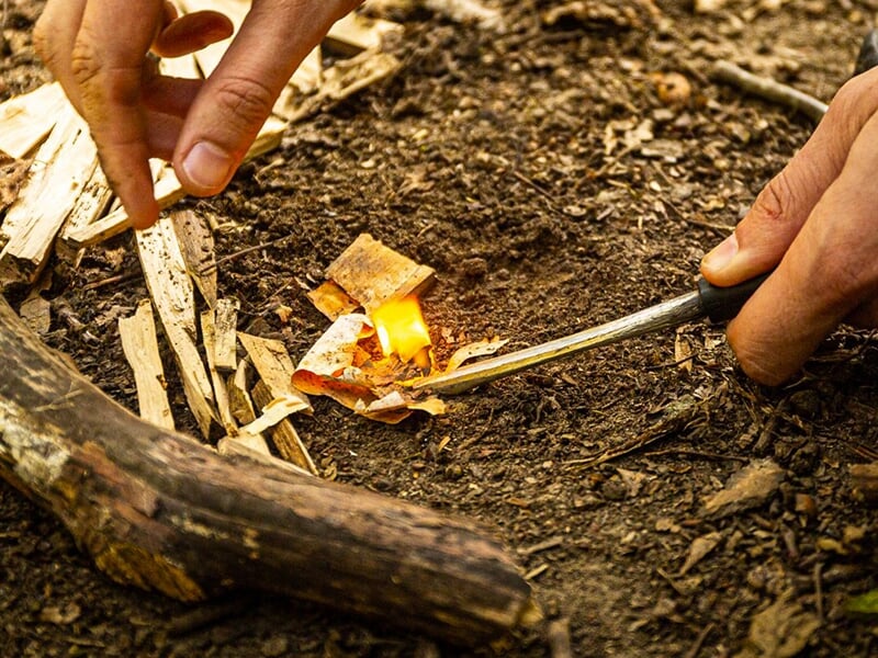 Mains utilisant une pierre à feu pour enflammer un petit tas d'écorces et de copeaux de bois.