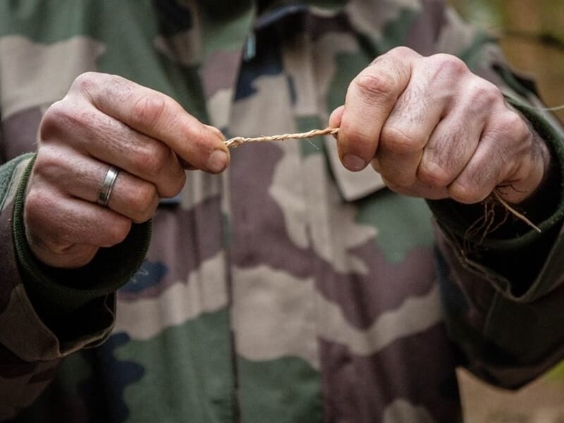 Personne en tenue camouflage tenant une cordelette entre ses mains lors d'un stage de survie dans les Vosges du Nord.