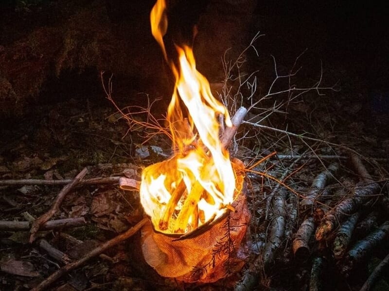 Feu de camp vif dans un récipient en métal lors d'un stage de survie dans les Vosges du Nord.