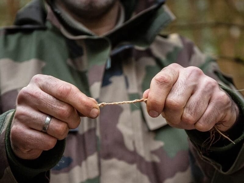 Gros plan sur les mains d'une personne en tenue camouflage, tordant une cordelette en forêt