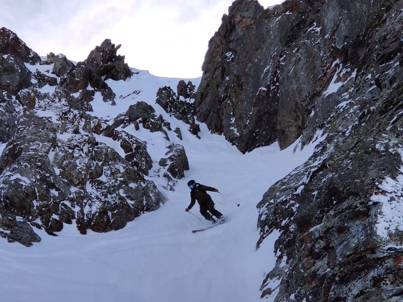 Skieur descendant une pente raide entre des rochers enneigés dans les montagnes des Deux Alpes.
