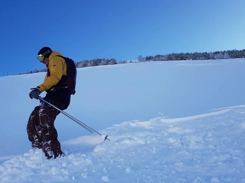 Personne en tenue jaune et marron pratiquant le ski de randonnée sur une neige fraîche sous un ciel bleu.
