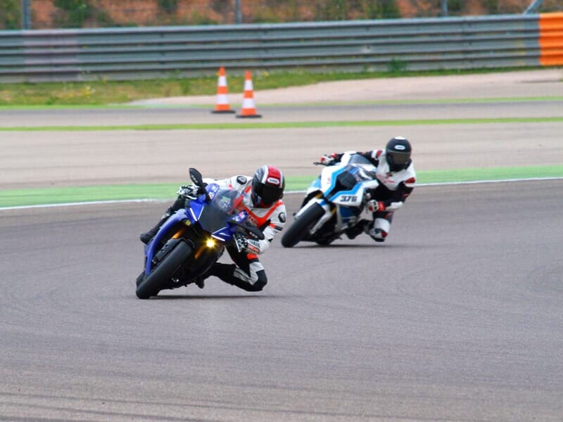 Deux motards en tenue de course prennent un virage sur la piste, l'un sur une Yamaha bleue et l'autre sur une moto blanche et noire