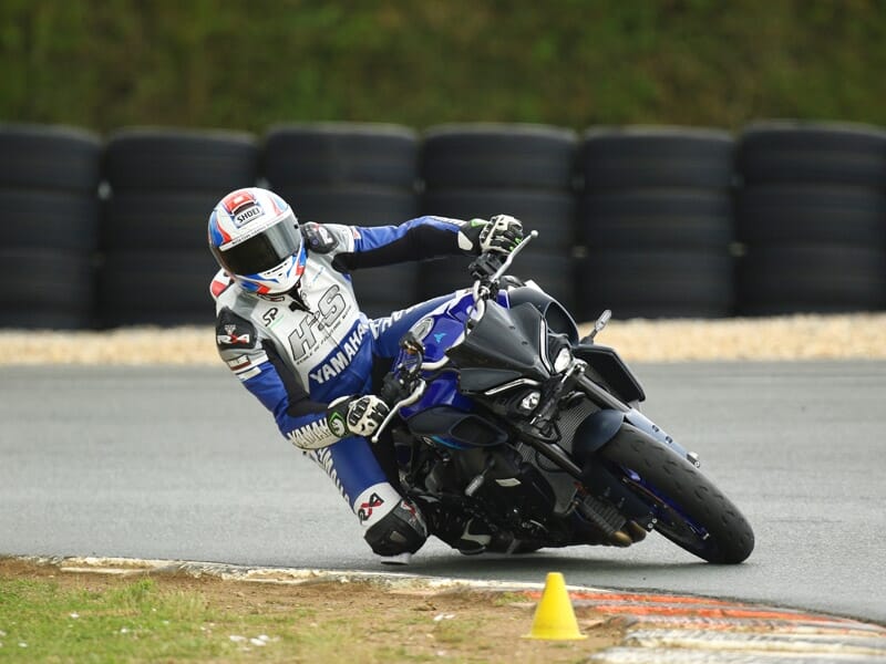 Pilote de moto en tenue de course bleue et blanche prenant un virage serré sur une Yamaha noire lors d'une journée de piste