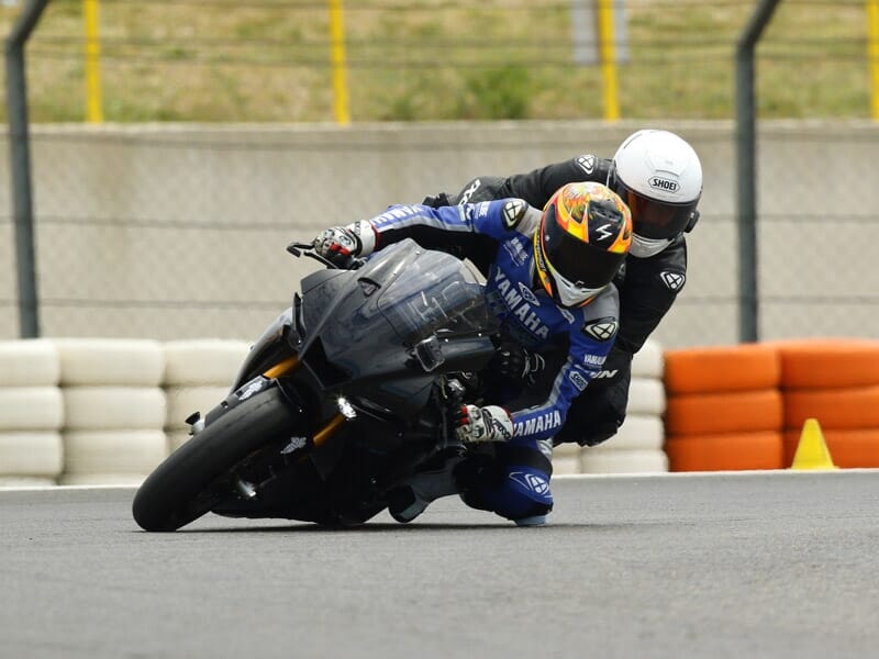 Pilote de moto en combinaison de course Yamaha prenant un virage serré sur une moto sportive noire sur un circuit de course, concentré sur la piste devant lui