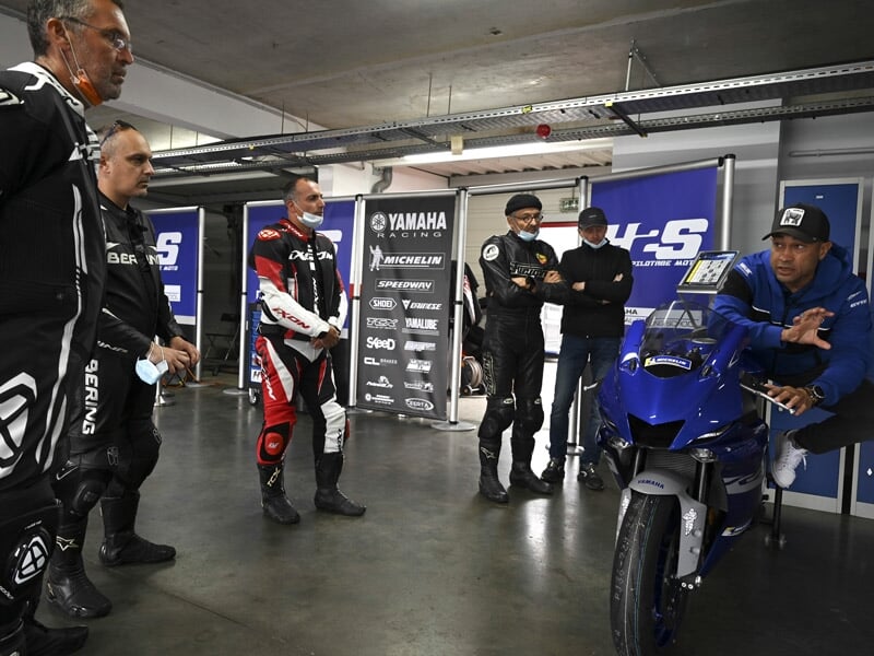 Groupe de motards en équipement de course écoutant un briefing dans un garage de circuit de course