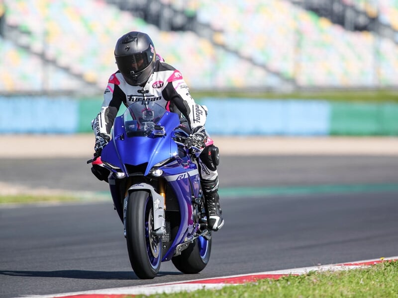 Pilote de moto en tenue de course Ixon se tenant à côté de sa moto sportive Yamaha bleue sur la piste