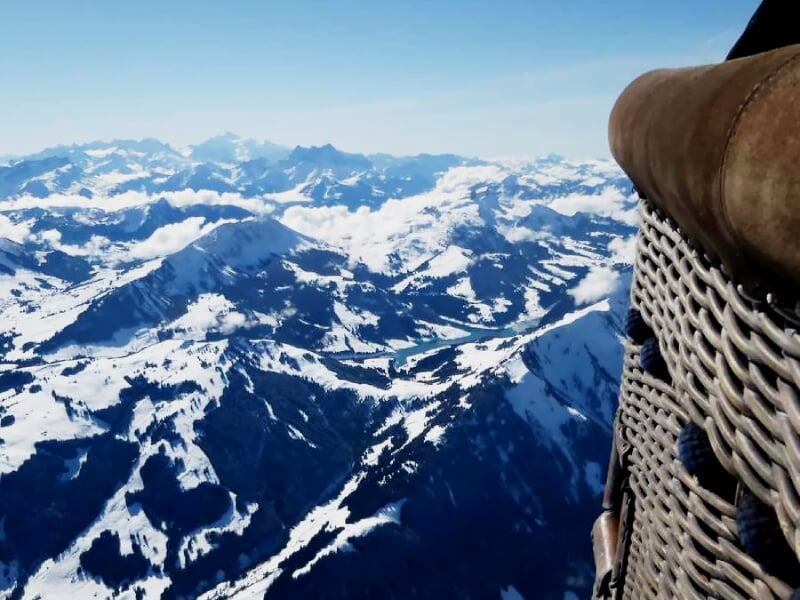Vue aérienne des montagnes enneigées depuis une montgolfière avec la nacelle visible au premier plan.