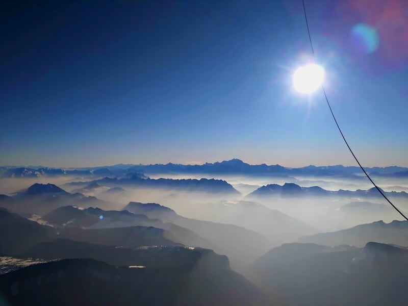 Paysage de montagnes embrumées sous un ciel bleu avec le soleil brillant, vu depuis une montgolfière.