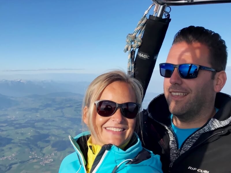 Couple souriant portant des lunettes de soleil dans la nacelle d'une montgolfière en vol.