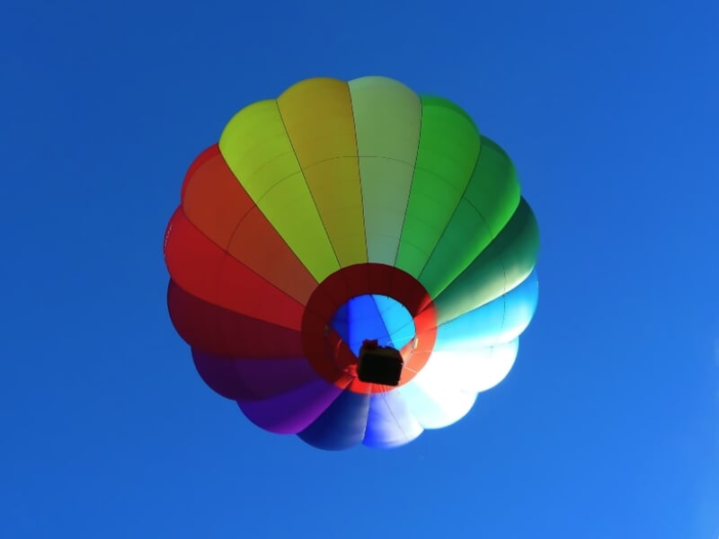 Montgolfière colorée vue du dessous, flottant dans un ciel bleu sans nuages.