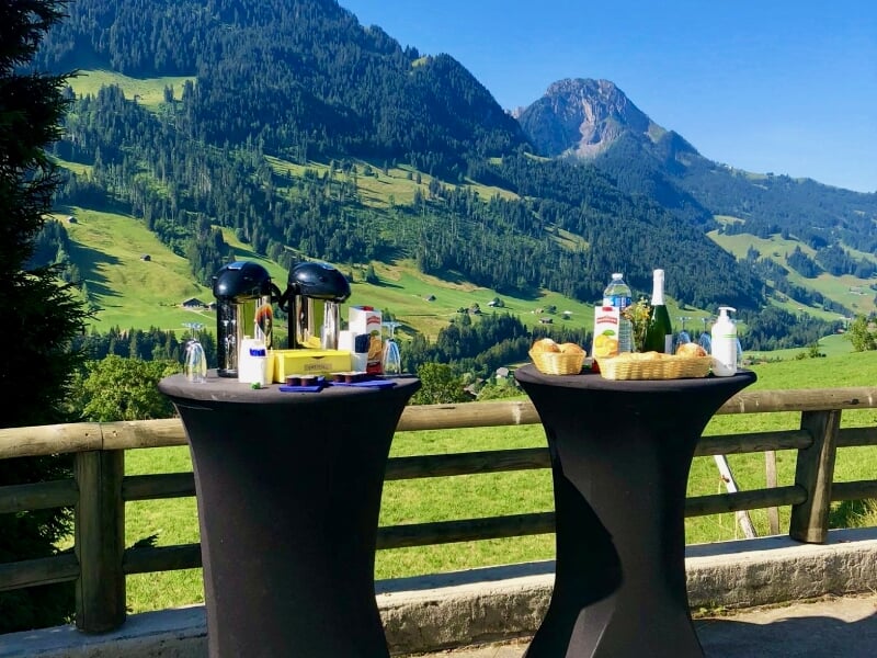 Deux tables hautes avec boissons et collations sur une terrasse avec vue sur la montagne.