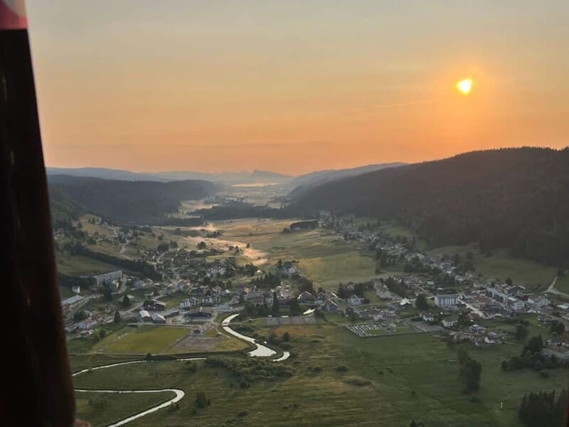Vue aérienne d'un village entouré de collines verdoyantes au coucher du soleil, lors d'un vol en montgolfière près de Métabief.