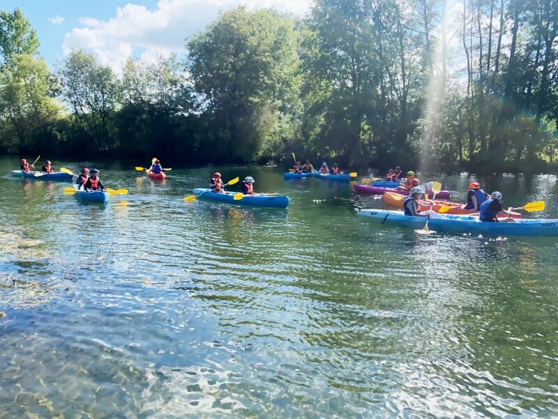 Groupe de personnes pagayant en kayak sur une rivière claire entourée d'arbres sous un ciel bleu lumineux.