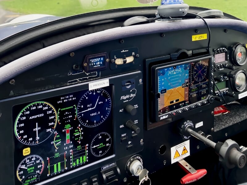 Cockpit d'un avion léger avec plusieurs instruments de vol et un écran numérique allumé.
