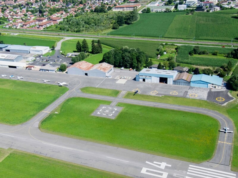 Vue aérienne d'un aérodrome avec une piste d'atterrissage, des hangars et des avions au sol.