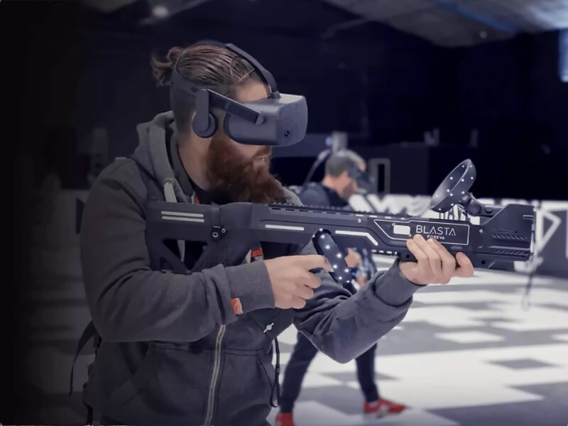 Homme avec casque de réalité virtuelle jouant à un jeu de tir avec une arme futuriste dans un espace sombre.