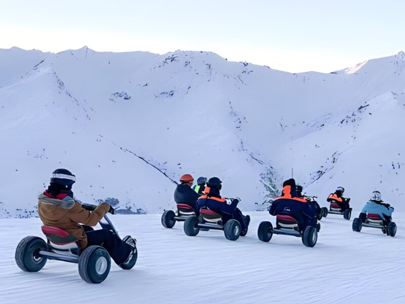 Groupe de personnes conduisant des karts tout-terrain sur un chemin enneigé en montagne.