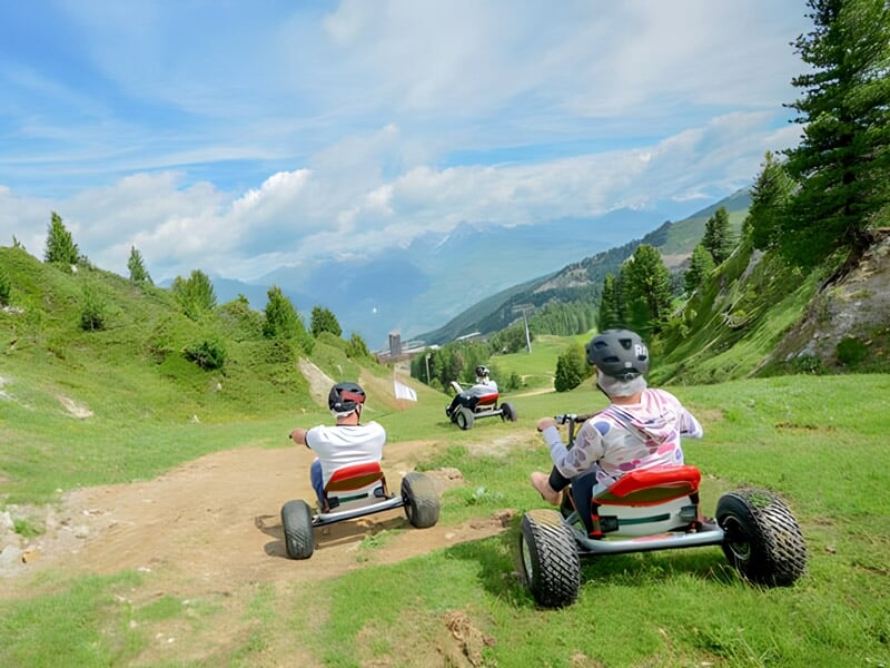 Personnes en karts tout-terrain roulant sur un sentier de montagne entouré de verdure.