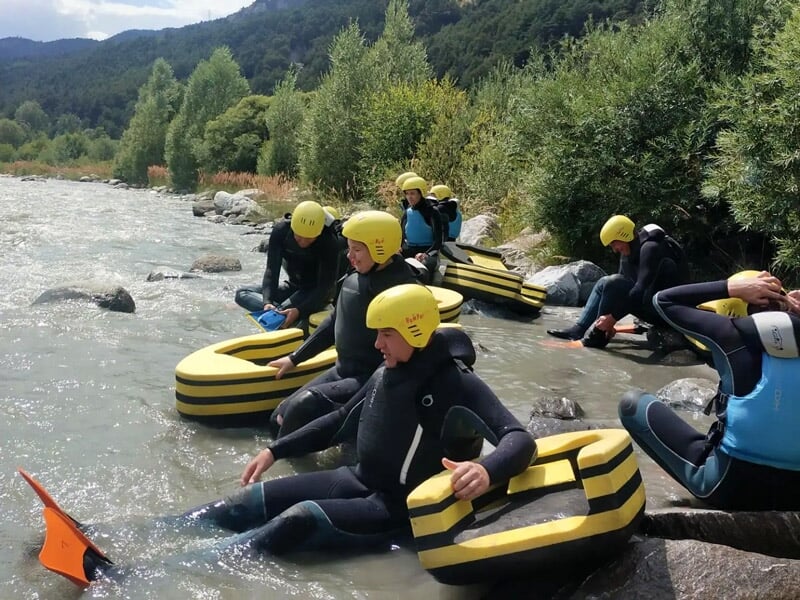 Groupe de personnes en combinaison noire et casque jaune assises au bord d'une rivière pour hydrospeed.