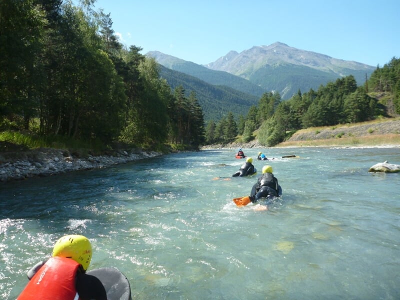 Personnes en hydrospeed descendant une rivière entourée de forêt et montagnes au loin.