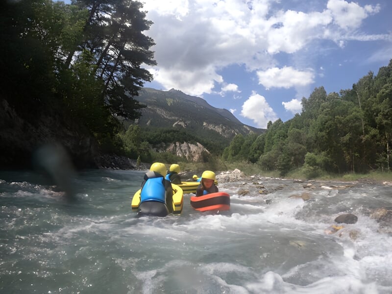 Deux personnes en hydrospeed naviguant sur une rivière avec des rapides et des rochers.
