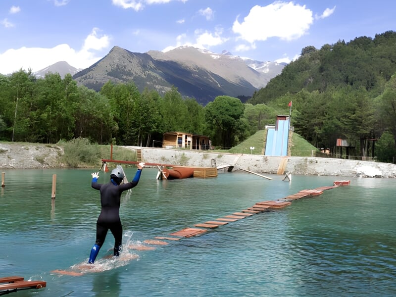 Personne marchant sur des planches flottantes dans un parc aquatique avec montagnes en arrière-plan.