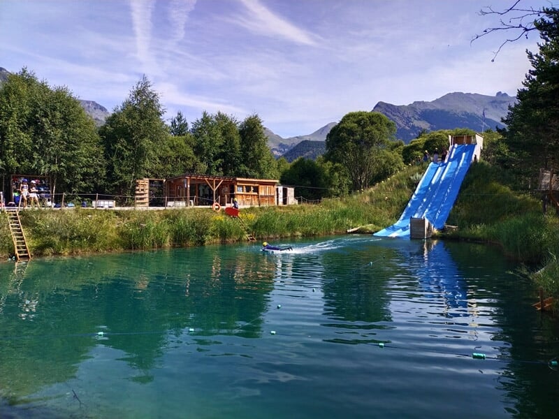 Vue d'un toboggan bleu dans un parc aquatique avec un bassin d'eau et montagnes en arrière-plan.